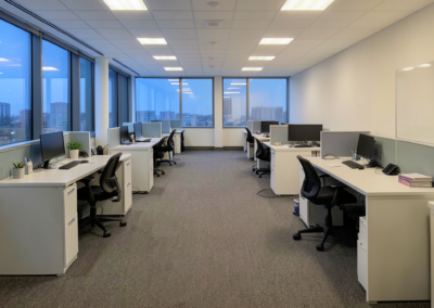 Open-plan office with vacuumed carpet, tidy desks, and clear walkways after evening commercial cleaning.